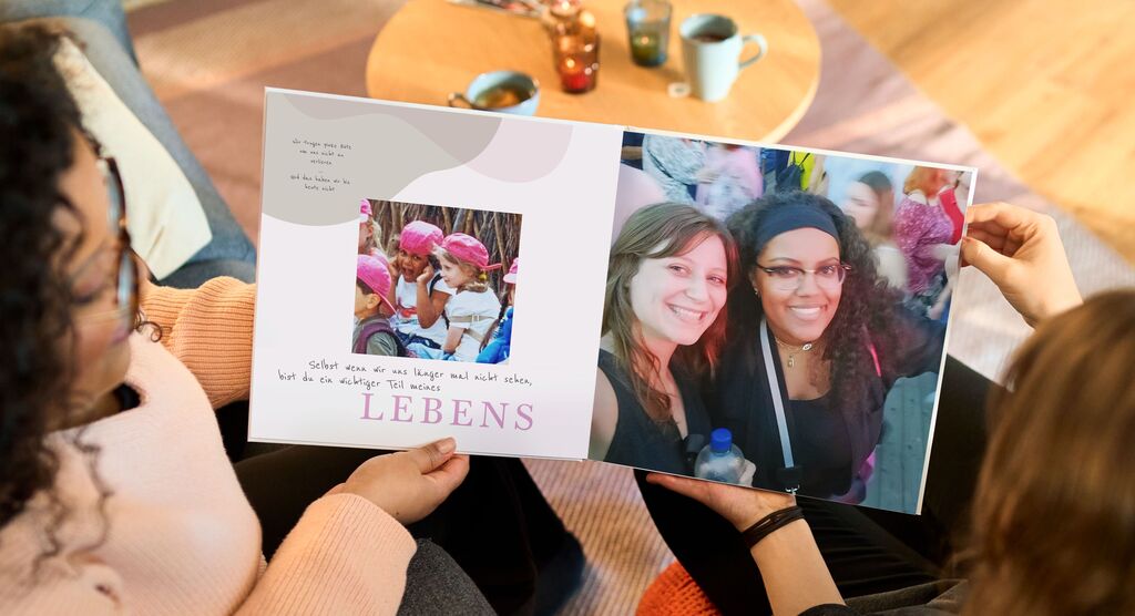 Zwei Personen zeigen ein geöffnetes Fotobuch mit bunten Erinnerungen.