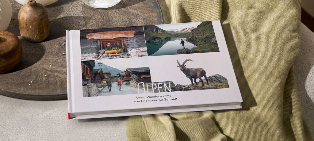 Ein CEWE FOTOBUCH mit Themenbildern aus den Alpen, das auf einem Holztisch liegt.