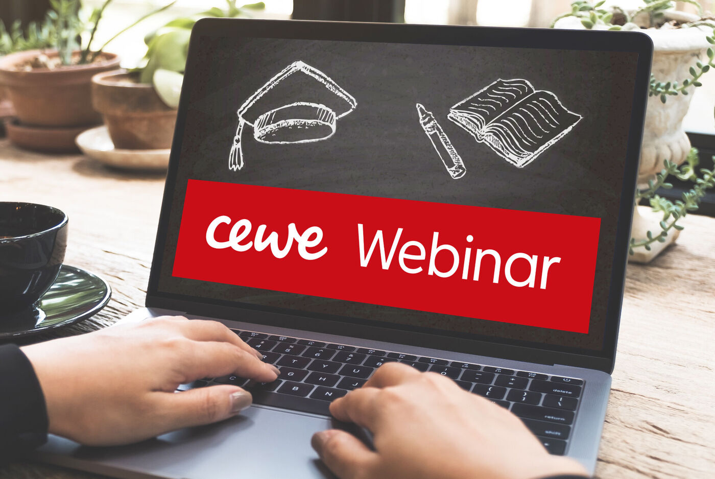 Hände tippen auf ein Laptop, das einen CEWE Webinar Schriftzug zeigt.