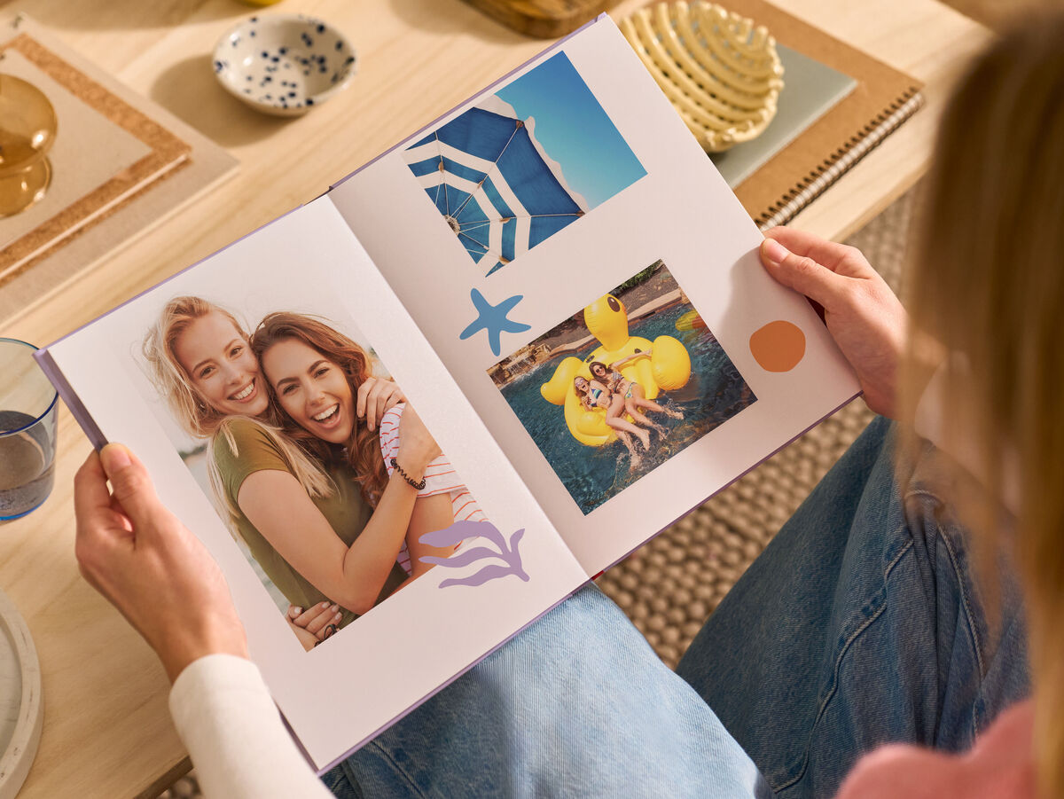 Eine Frau sitzt im Wohnzimmer auf einem Sofa, in ihren Händen hält sie ein aufgeschlagenes CEWE FOTOBUCH.