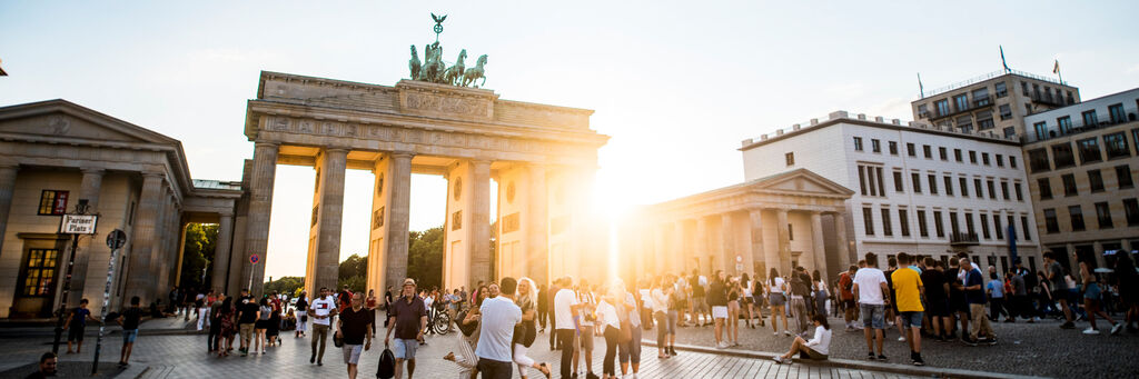 Menschen versammeln sich vor dem Brandenburger Tor in Berlin bei Sonnenuntergang.