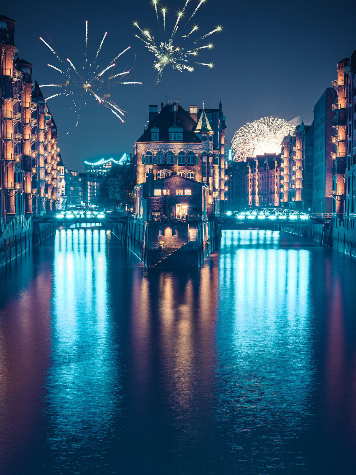 Blick auf ein beleuchtetes Gebäude am Wasser, umgeben von Feuerwerk.