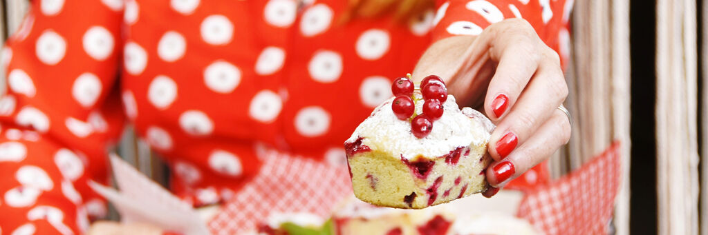 Eine Frau mit rotem Polka-Dot-Oberteil hält einen Kuchen mit roten Johannisbeeren in der Hand.