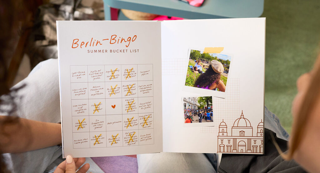 Zwei Frauen halten gemeinsam ein CEWE FOTOBUCH. Sie betrachten eine Doppelseite, auf der ein Bingo-Feld zu sehen ist.