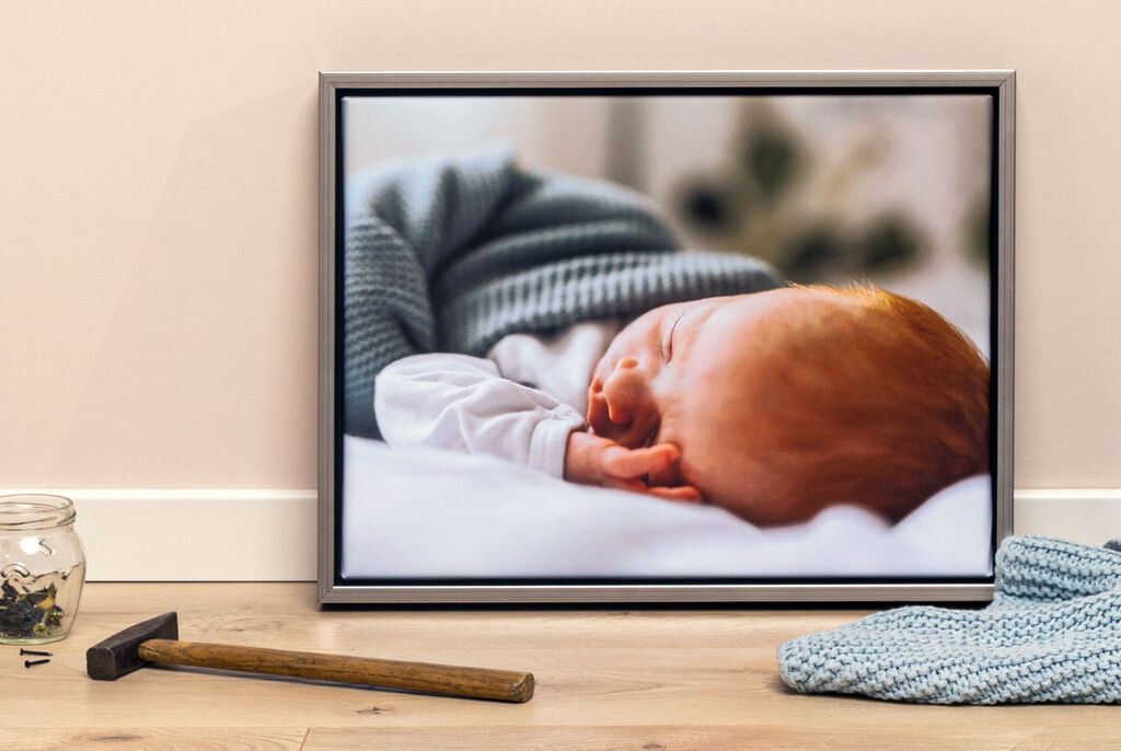 Ein schlafendes Baby auf einem Bett, eingehüllt in einer weichen Decke. Die rotschöpfigen Haare sind sichtbar und das Baby hat eine ruhige Handhaltung.