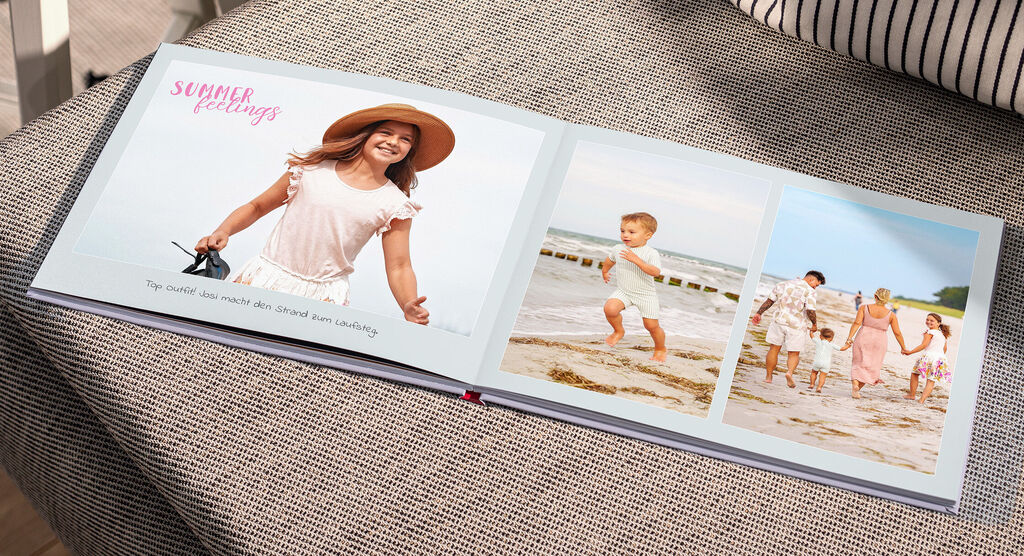 Ein CEWE FOTOBUCH liegt auf dem Sofa. Darin sind Fotos von einer Familie am Strand zu sehen.