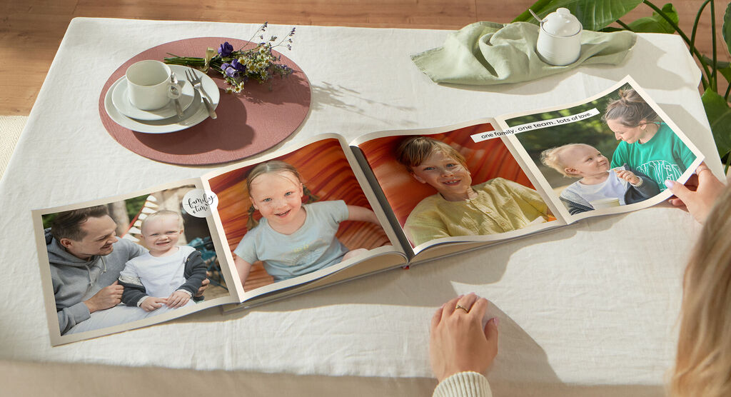 Eine Person blättert durch ein CEWE Fotobuch auf einem Tisch mit einer Tasse und einem Blumenarrangement