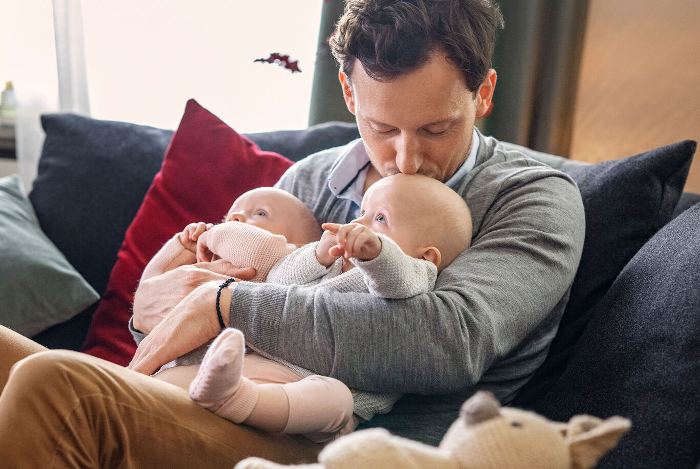 Ein liebevoller Moment mit zwei Babys, die in den Armen ihres Vaters sitzen und niedlich schauen.