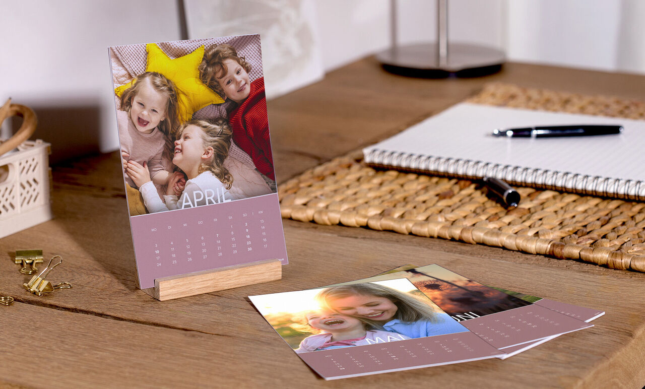 Ein farbenfroher Tisch mit einem CEWE Fotokalender, Bildern von glücklichen Momenten und süßen Erinnerungen.