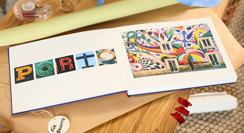 Offenes CEWE FOTOBUCH mit buntem Wandbild und Buchstaben-Collage auf Holztisch.