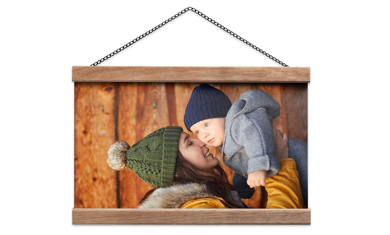 Eine lächelnde Mutter hält ihr Baby in warmer Kleidung vor einer Holzwand.