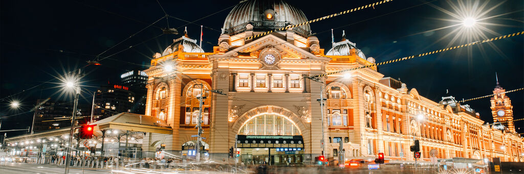 Schön beleuchtet, das historische Flinders Street Station Gebäude in Melbourne bei Nacht, umgeben von Lichtern.