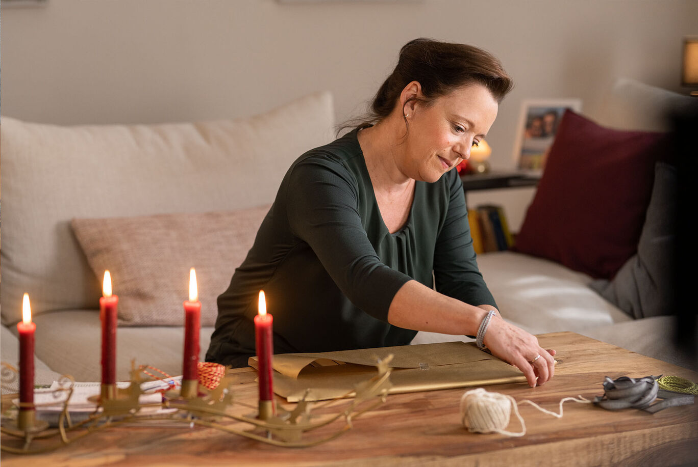 Eine Person verpackt liebevoll ein Geschenk auf einem Holztisch, umgeben von Kerzen.