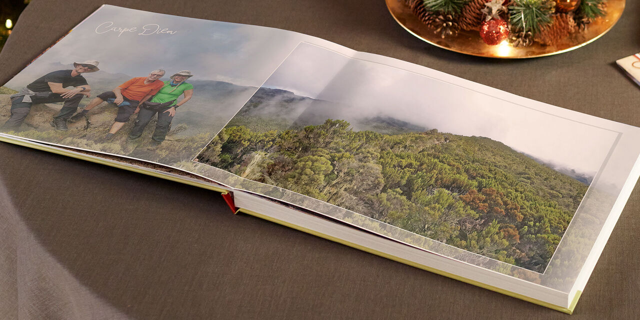 Offenes CEWE Fotobuch mit einer Landschaftsaufnahme und drei Personen auf einer Bergwiese.