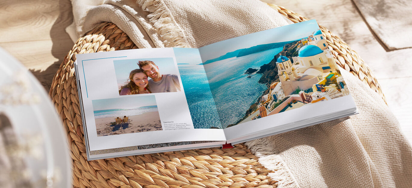 Ein offenes Fotobuch liegt auf einer Decke. Darin sind zwei Seiten mit Fotos von einem schönen Urlaub am Meer.