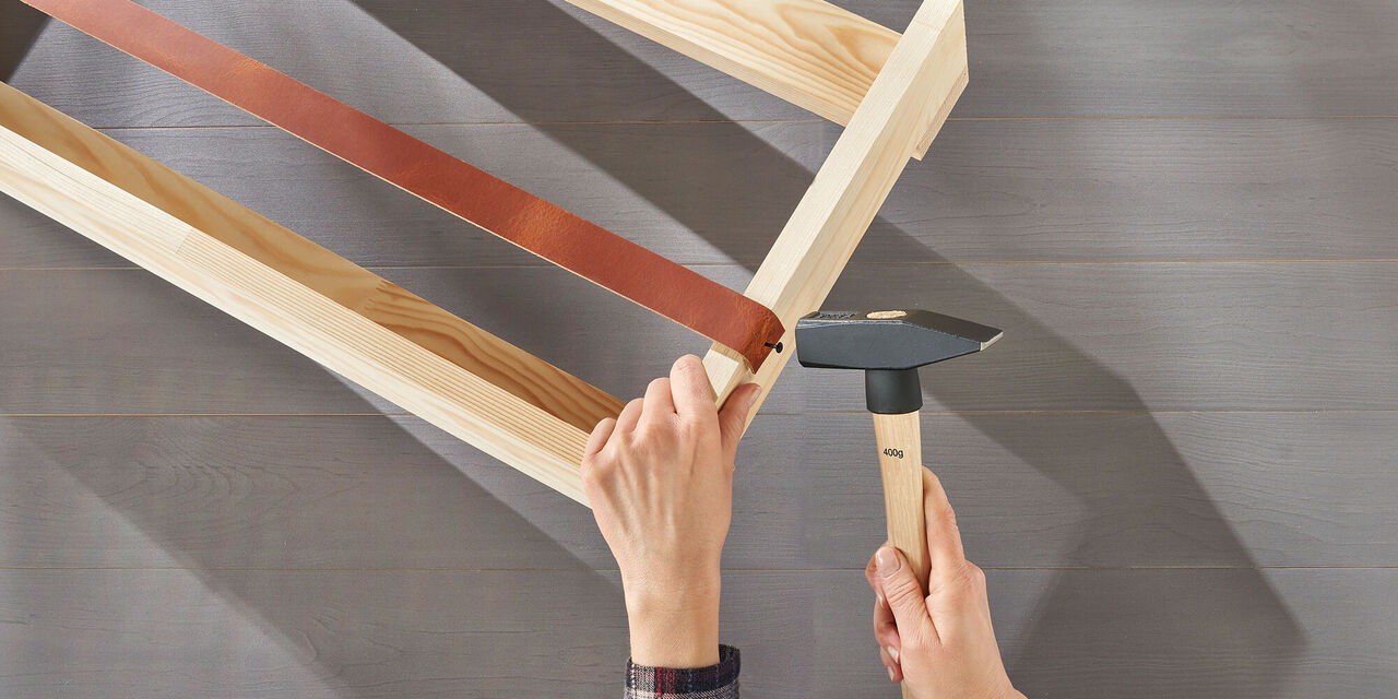 Hände montieren ein Holzgestell mit einem Hammer und einem Lederband