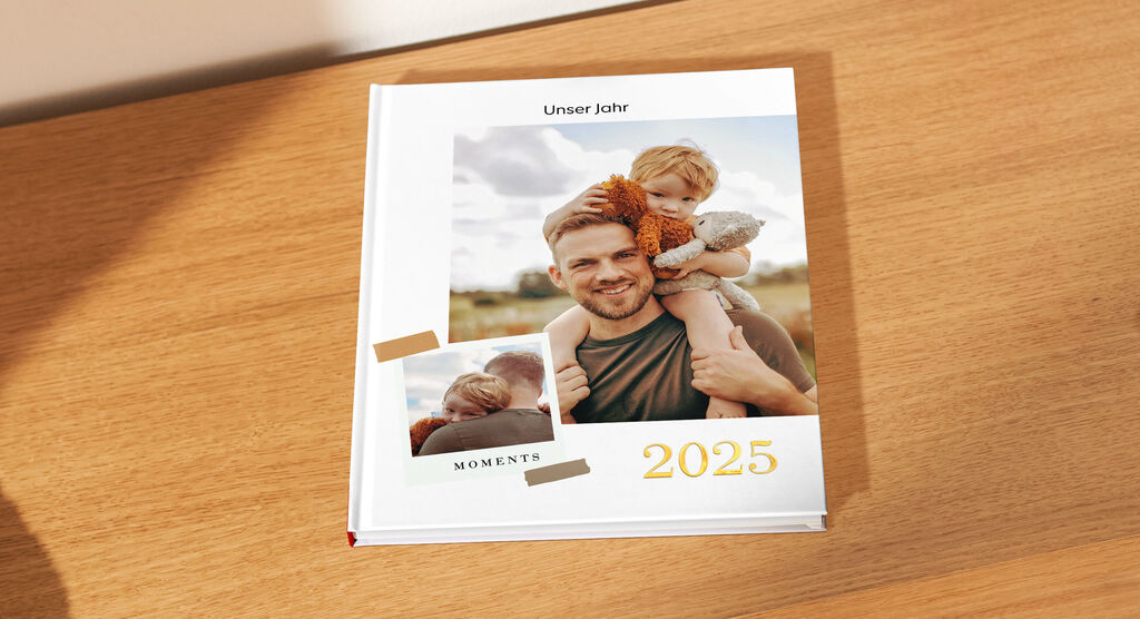 Ein Fotobuch mit dem Titel 'Unser Jahr 2024' auf einem Holztisch. Es zeigt glückliche Momente und ist liebevoll gestaltet.
