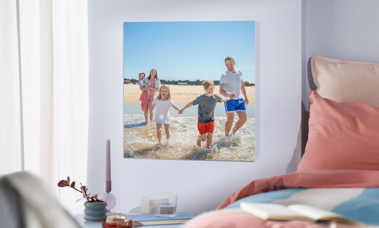 Eine glückliche Familie spielt im Wasser am Strand. Zwei Erwachsene und zwei Kinder halten Händchen. Sonnenlicht strahlt auf sie.