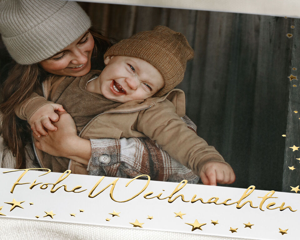 Ein schöner Schnappschuss mit einer Mutter, die ihr Kind liebevoll umarmt, im Hintergrund eine holzige Kulisse, perfekt für Weihnachtsgrüße.