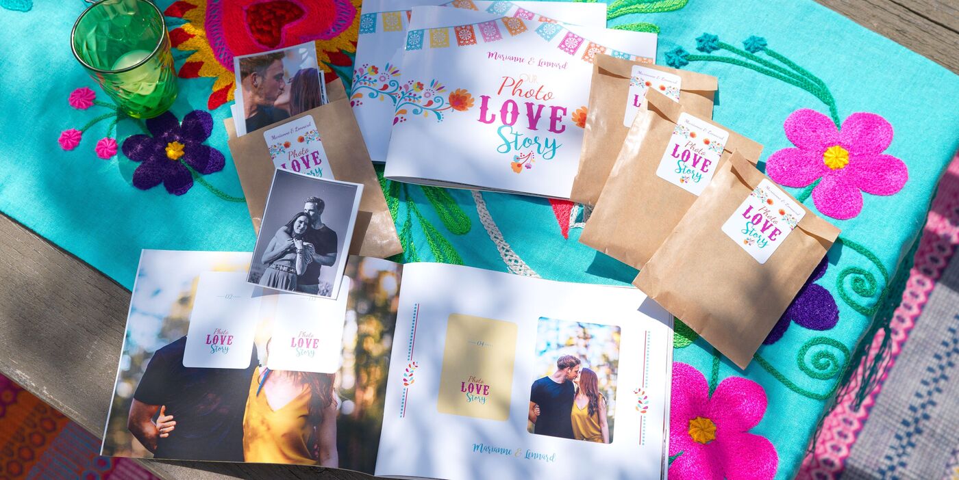 Offenes CEWE FOTOBUCH mit Titel Photo Love Story, dazu Fotos und kleine braune Tüten auf bunter Decke
