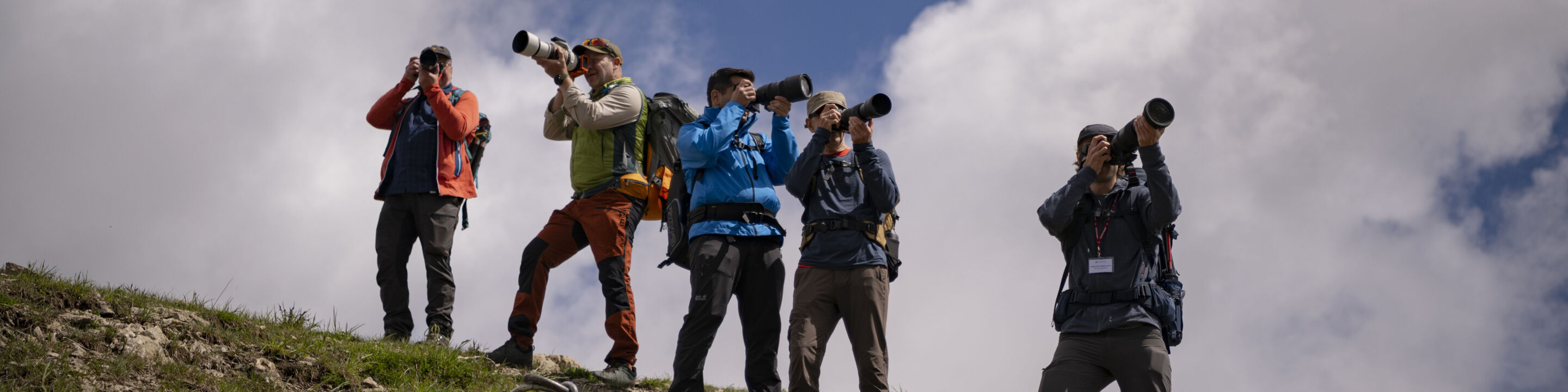 Fünf Personen stehen auf einem Hügel und fotografieren die Umgebung mit großen Kameraobjektiven.