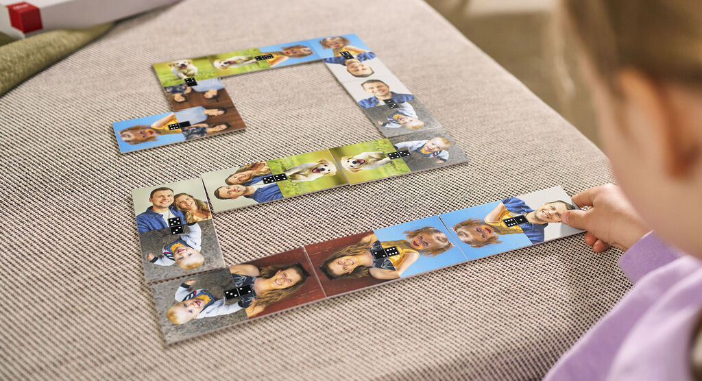 Ein Kind spielt mit einem personalisierten Fotopuzzle, das aus Bildern von glücklichen Momenten besteht. Es ist auf einem hellen Sofa arrangiert.