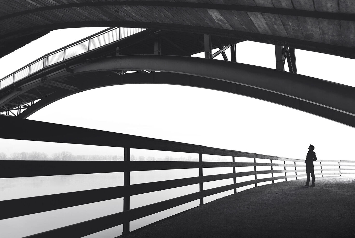 Silhouette einer Person unter einer geschwungenen Brücke in Schwarz-Weiß