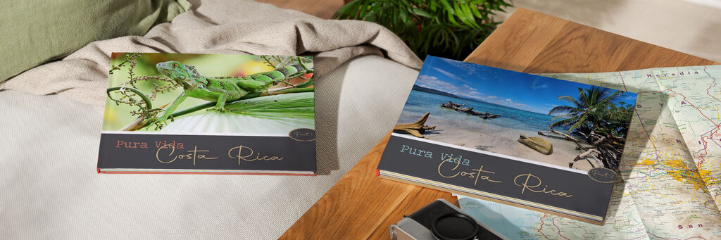 Zwei wunderschöne Fotobücher über Costa Rica liegen auf einem Tisch, umgeben von einem Mappe und einer Kamera.