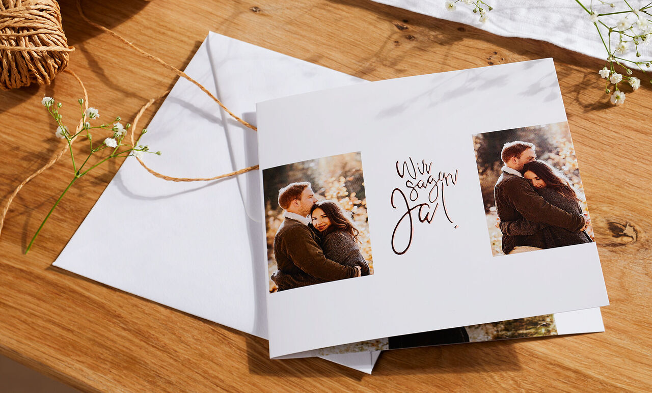 Zwei Menschen umarmen sich liebevoll vor einem Fotobuch mit dem Titel 'Wir sagen Ja'.