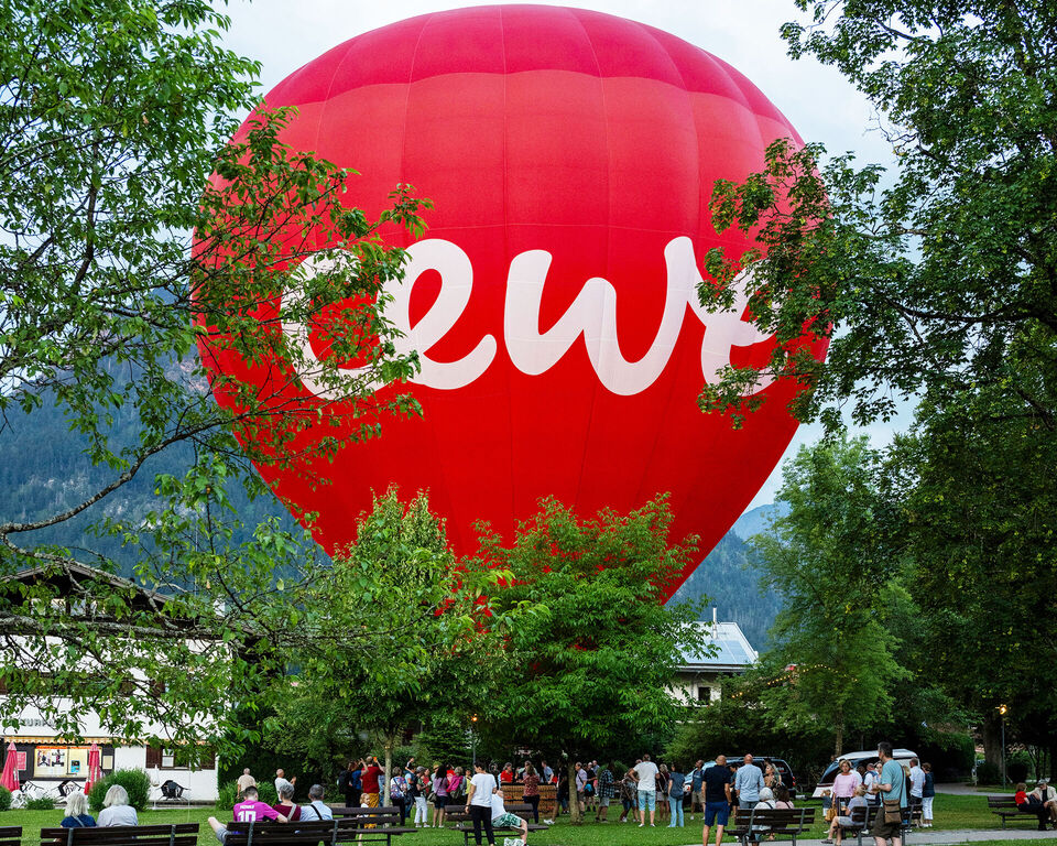 Im Vordergrund ist eine grüne Wiese. Im Hintergrund sieht man einen großen roten Heißluftballon mit CEWE Schriftzug.