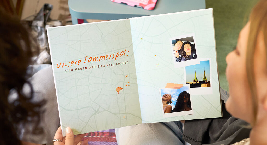 Zwei Frauen betrachten eine Doppelseite in einem CEWE FOTOBUCH, auf der eine Karte von Berlin zu sehen ist.