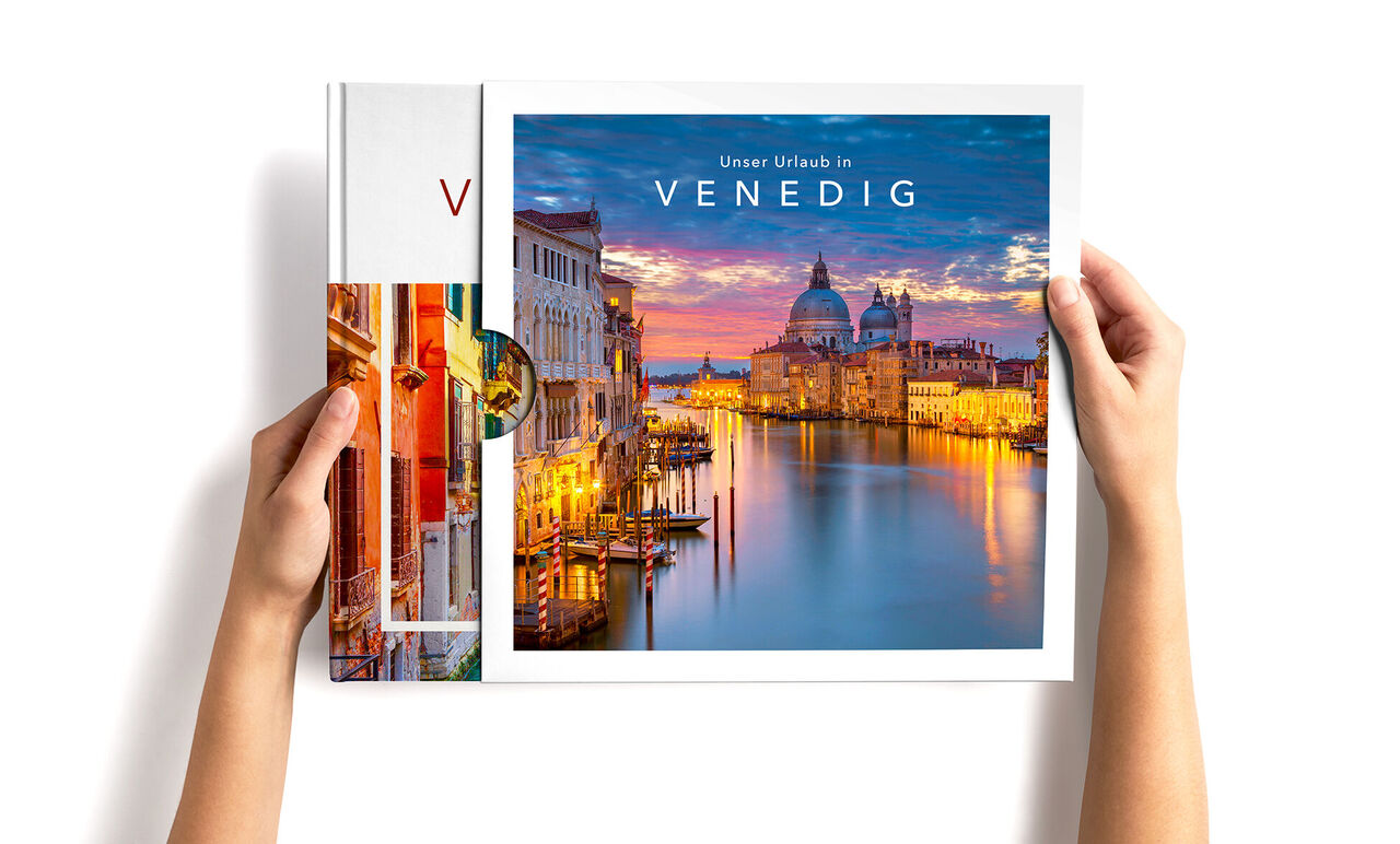 Person zieht ein CEWE FOTOBUCH Venedig mit farbenfrohen Stadtansichten aus einem Schuber