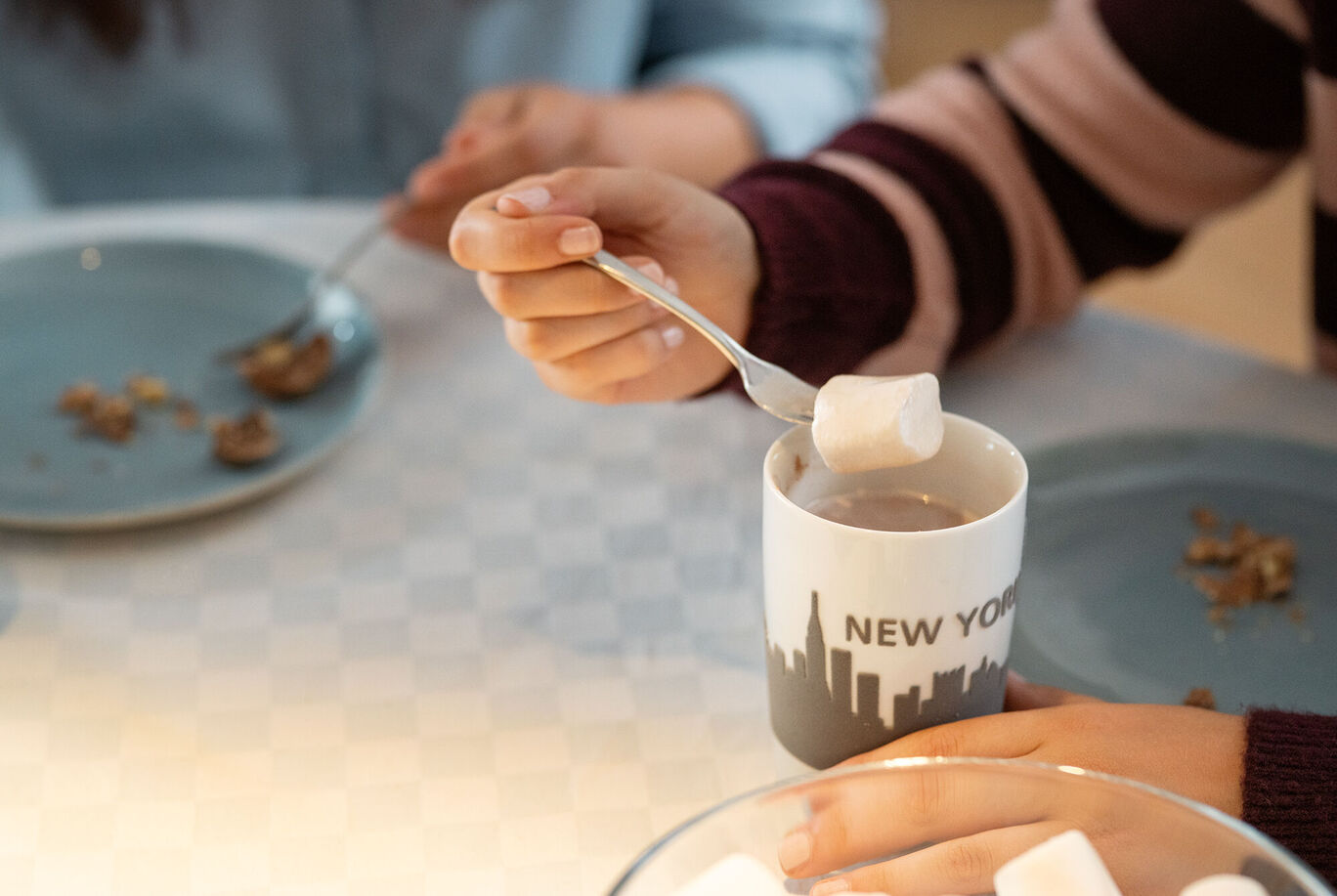 Personen genießen heiße Schokolade mit Marshmallows in einer Tasse mit Skyline-Design.