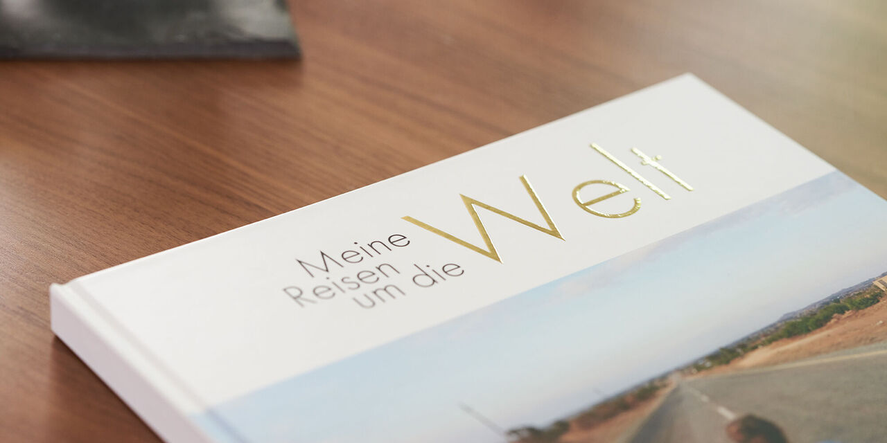 Ein CEWE Fotobuch mit dem Titel "Meine Reisen um die Welt" liegt auf einem Holztisch.