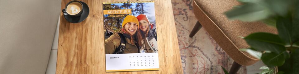 Kalender liegt auf Holztisch neben Kaffeetasse