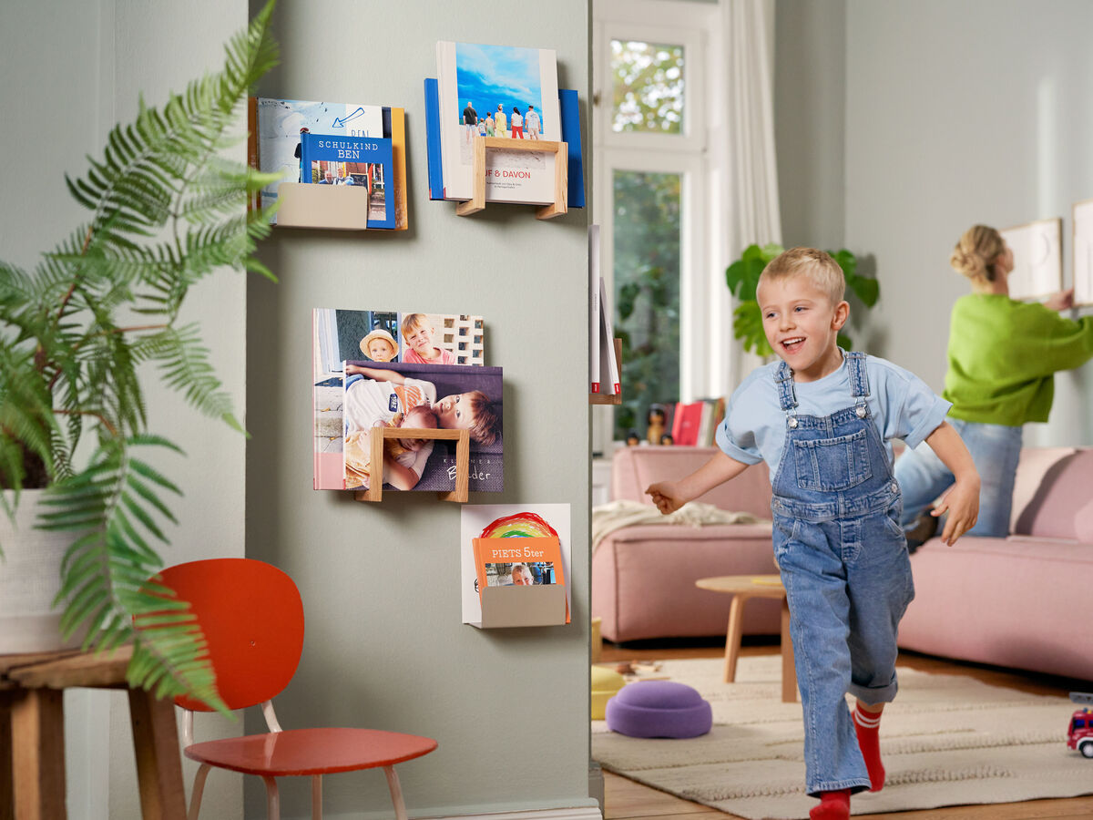 Ein Kind läuft in einem gemütlichen Wohnraum, während im Hintergrund wunderschöne Fotobücher an der Wand hängen. Sie schaffen eine kreative und inspirierende Atmosphäre.