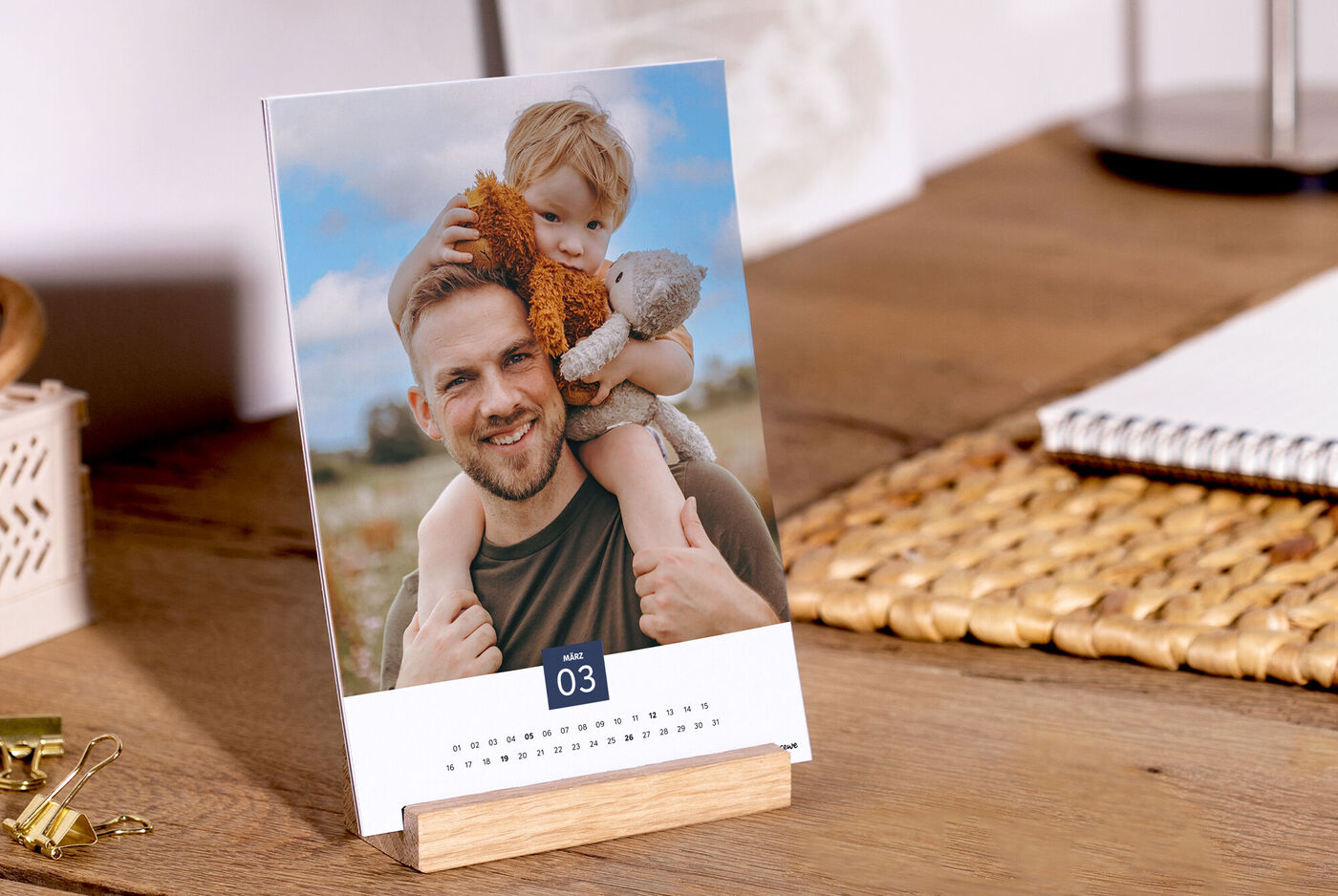 Ein attraktiver Fotokalender auf einem Tisch, der nachhaltigem Papier hergestellt ist. Ein Kind sitzt auf den Schultern eines Erwachsenen und hält ein Kuscheltier.