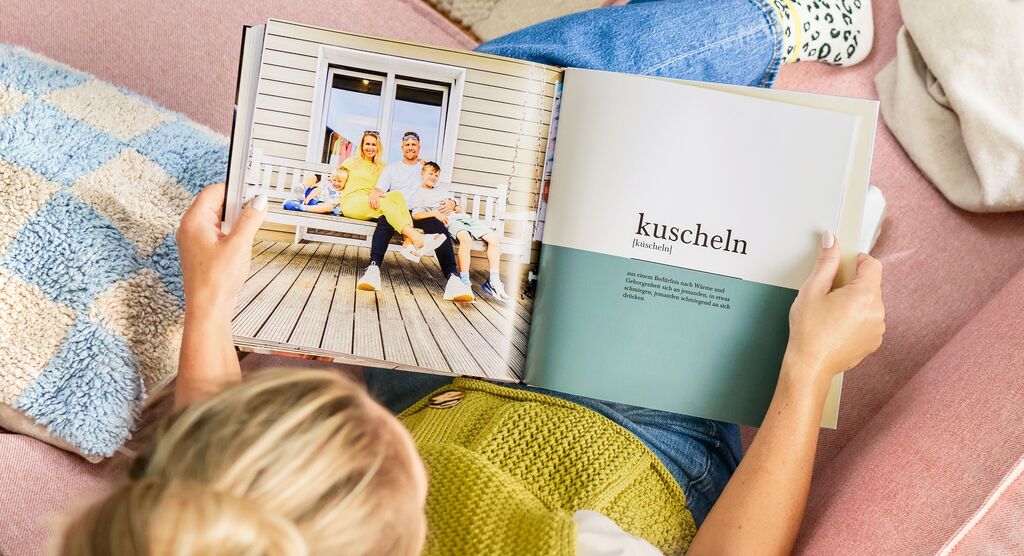 Eine Person blättert durch ein geöffnetes Fotobuch auf einem gemütlichen Sessel und betrachtet die Seite mit dem Wort "kuscheln".