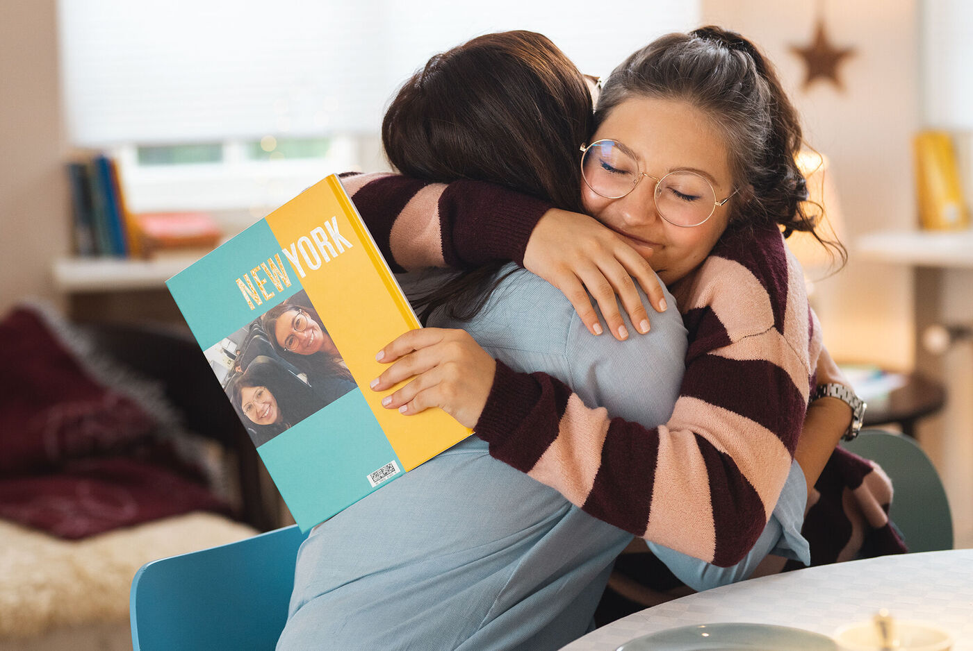 Zwei Frauen umarmen sich und halten ein CEWE Fotobuch mit dem Titel 'NEW YORK'.