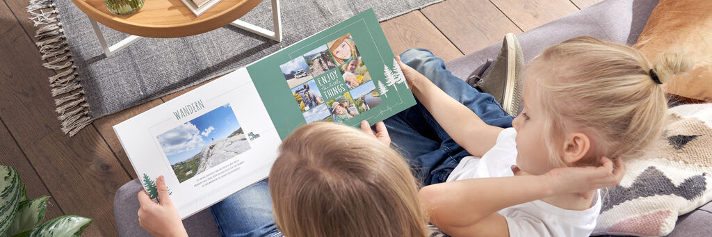 Zwei Kinder blättern in einem CEWE FOTOBUCH auf einem Sofa