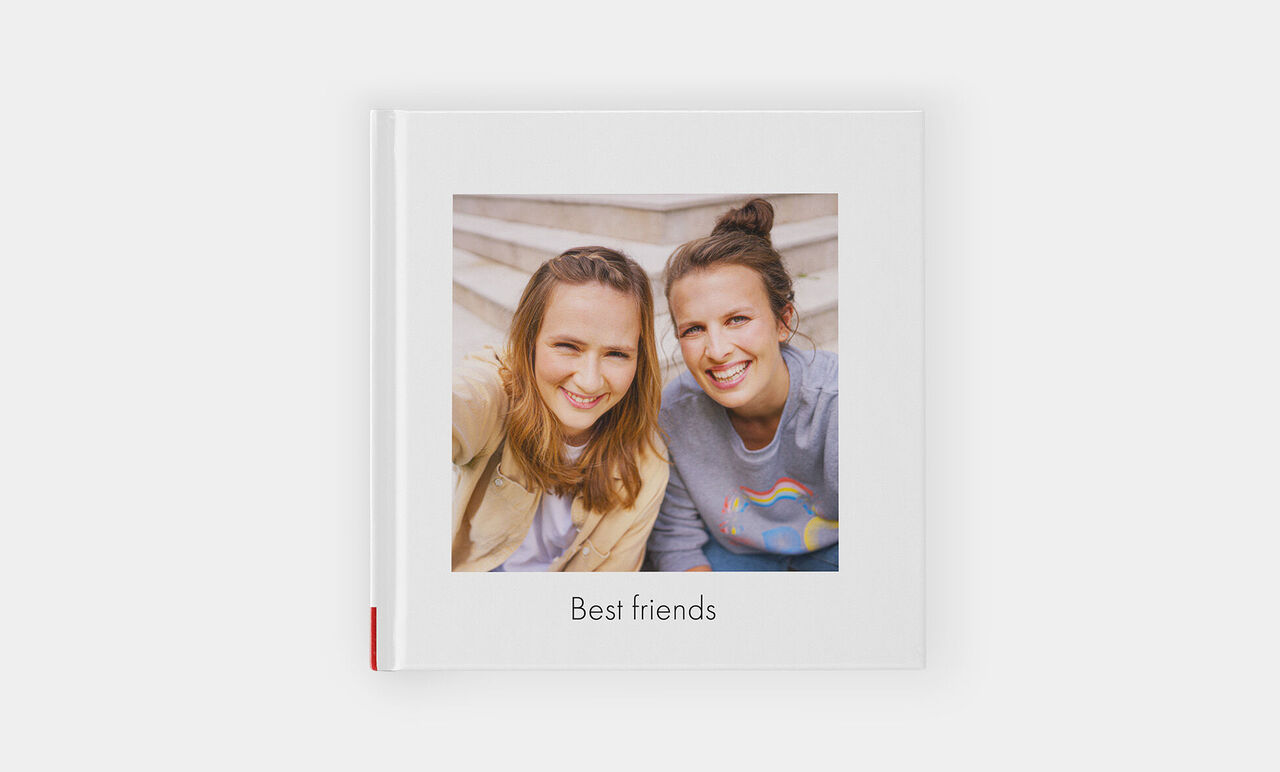 Zwei lächelnde Freundinnen halten ein Fotobuch mit dem Titel „Best Friends“.