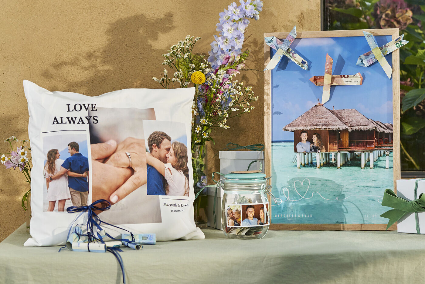 Kissen mit dem Text 'LOVE ALWAYS' und Fotos von Paaren, dazu ein dekoratives Bild von einem Strandbungalow.