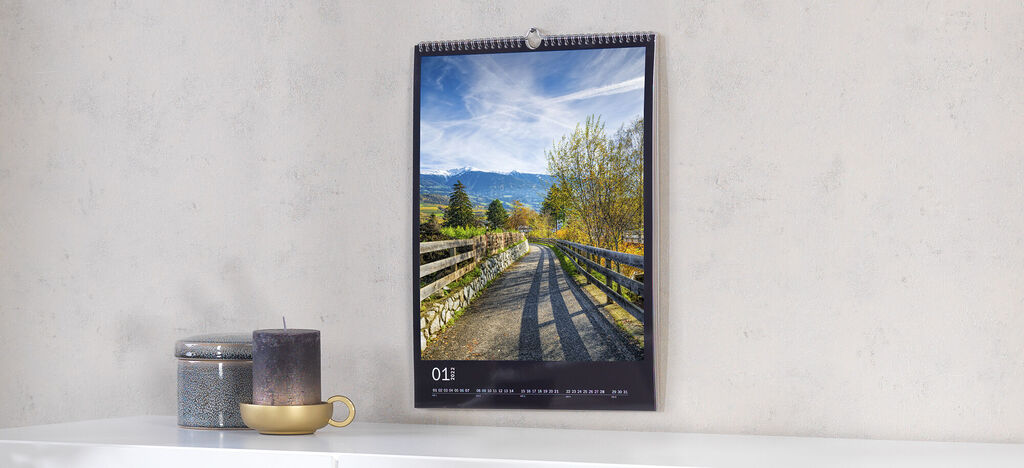 Ein Wandkalender mit einem schönen Landschaftsbild von einem Weg umgeben von Bäumen und Bergen im Hintergrund