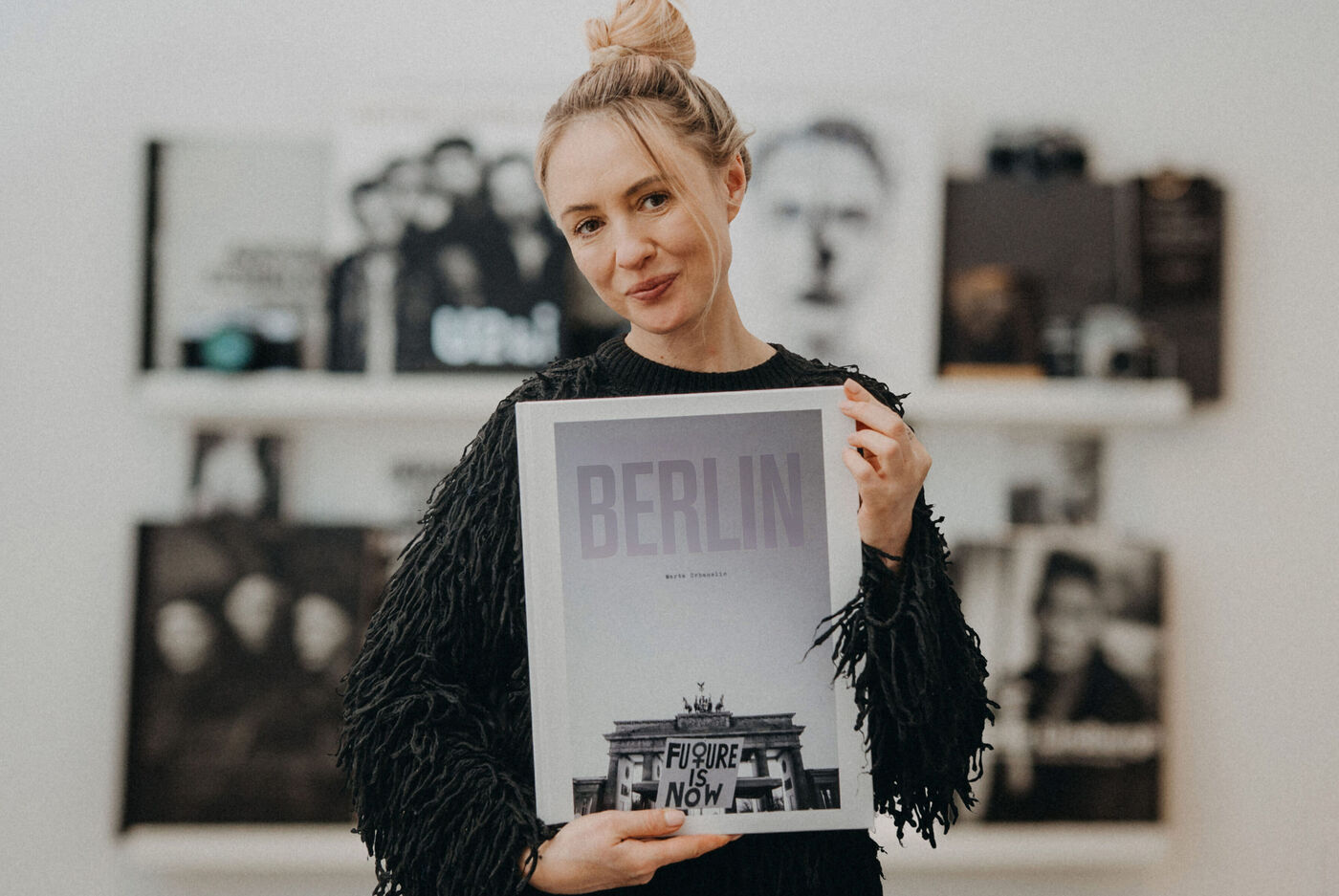 Marta Urbanelis steht vor ihrer Bücherwand und hält ein CEWE FOTOBUCH mit dem Titel "Berlin" in den Händen.