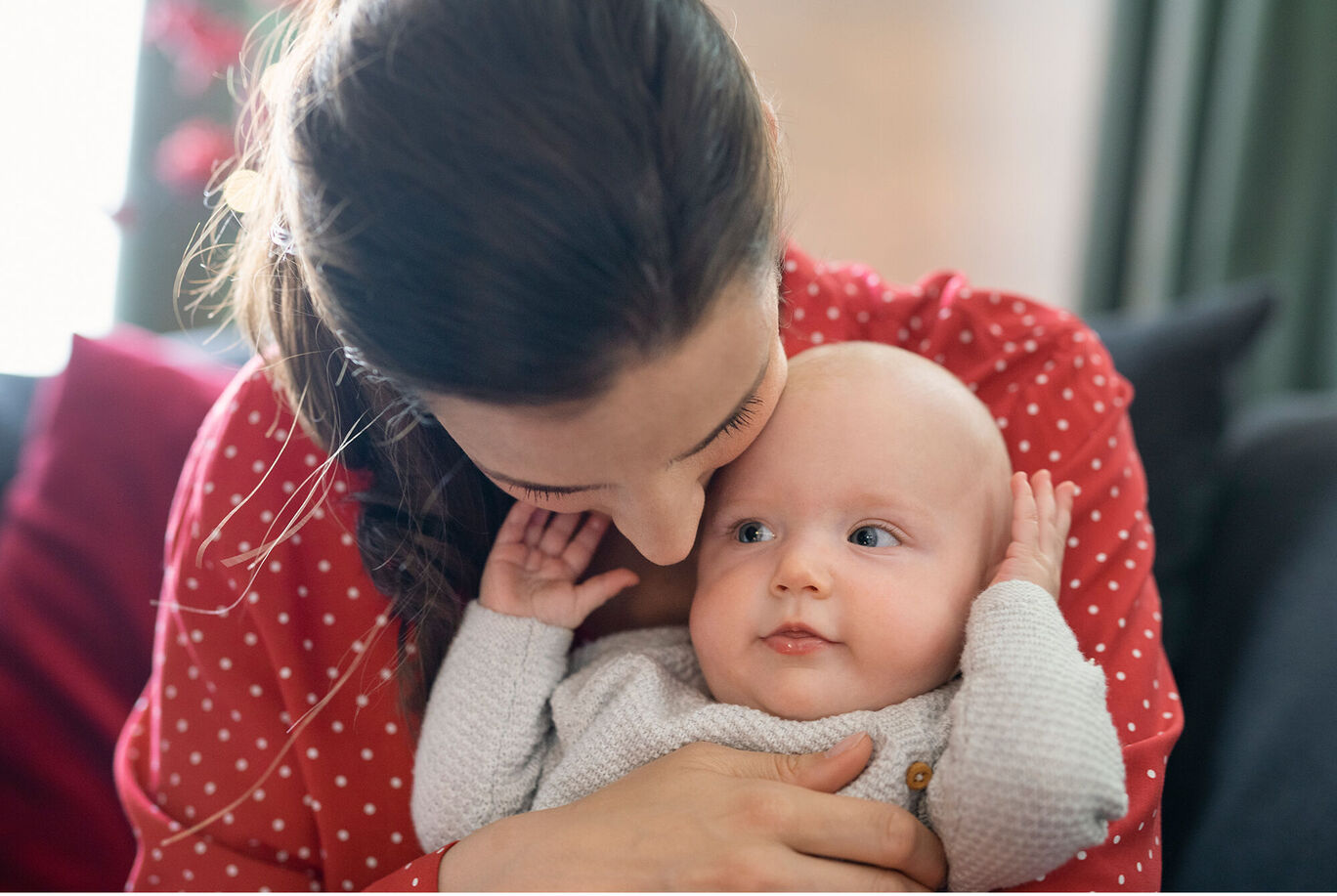Eine liebevolle Umarmung zwischen einer Mutter und ihrem Baby auf einer roten Couch, die Wärme und Nähe vermittelt
