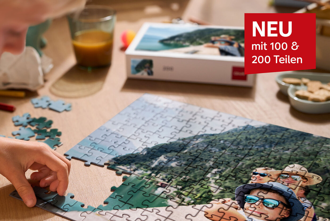 Eine Kinderhand setzt Puzzlestücke zusammen mit einer Landschaft und Personen auf dem Bild.