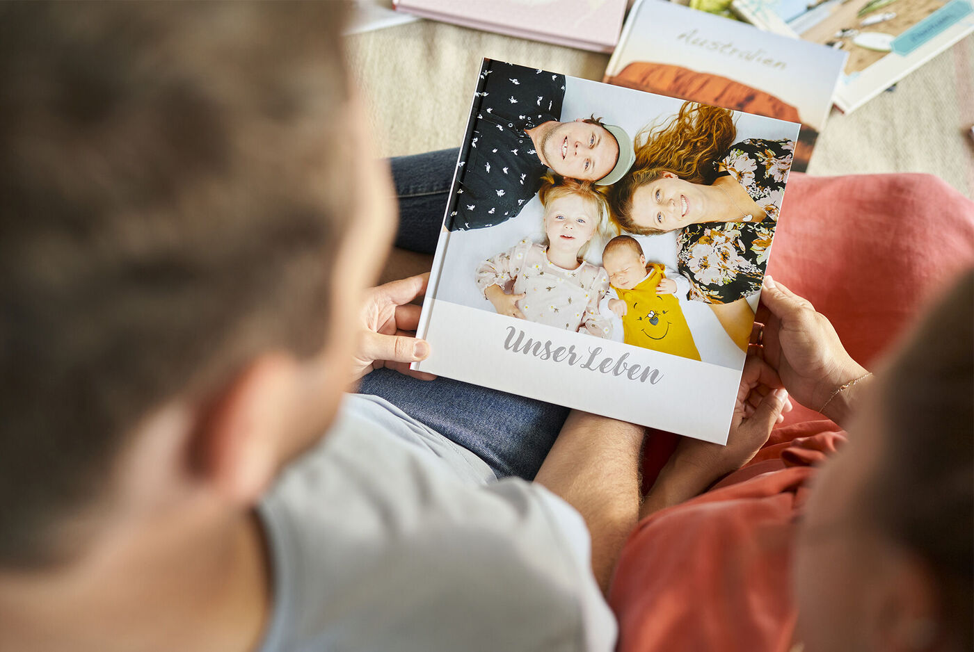 Ein Paar betrachtet gemeinsam ein CEWE FOTOBUCH mit dem Titel "Unser Leben". Das Buch zeigt Fotos von glücklichen Momenten und Erinnerungen.