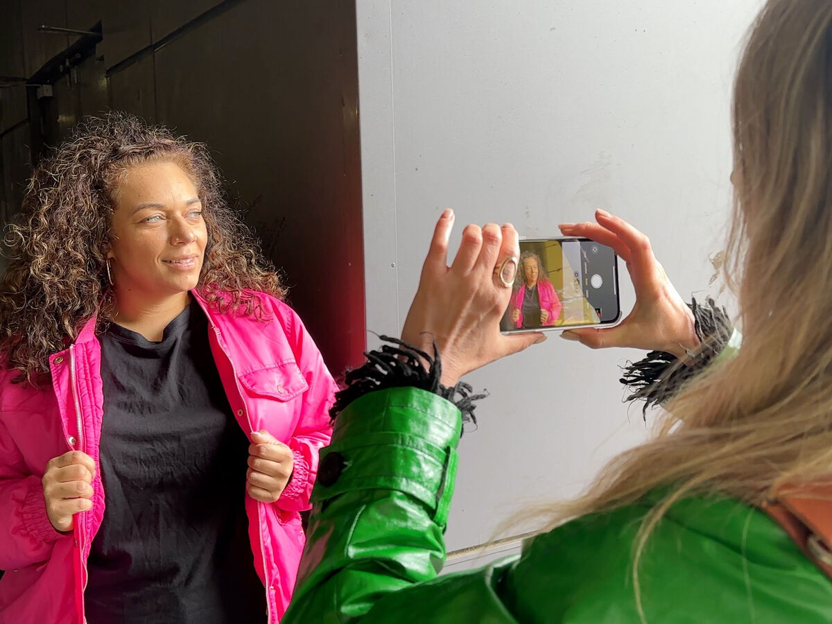 Zwei Frauen posieren fröhlich für ein Foto, eine trägt ein pinkes Outfit und die andere hält ein Smartphone.