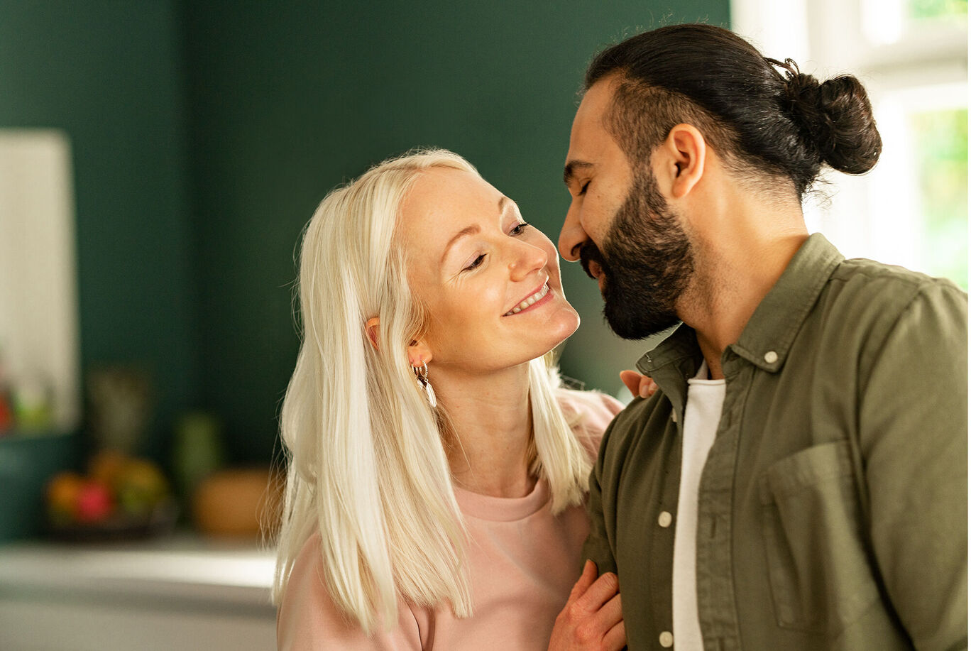Ein Paar mit blonden Haaren steht nah beieinander und genießt einen liebevollen Moment zusammen in einer modern eingerichteten Küche