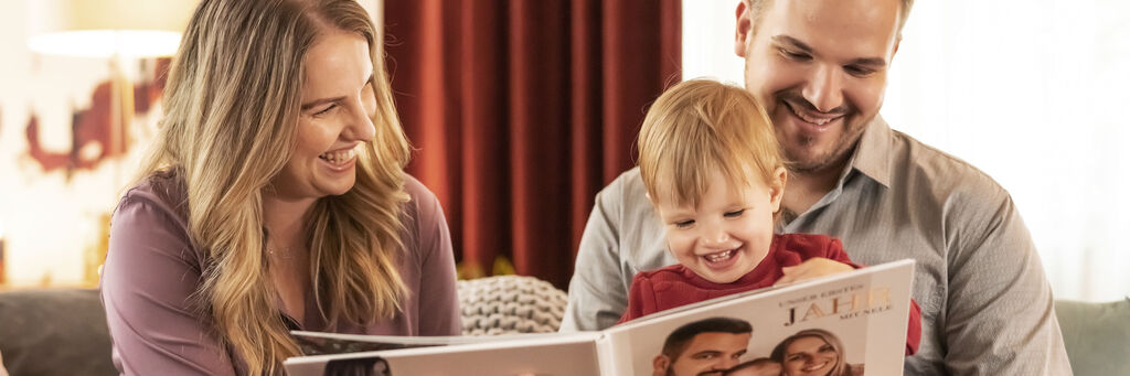 Eine Familie genießt gemeinsam ein CEWE FOTOBUCH auf dem Sofa.